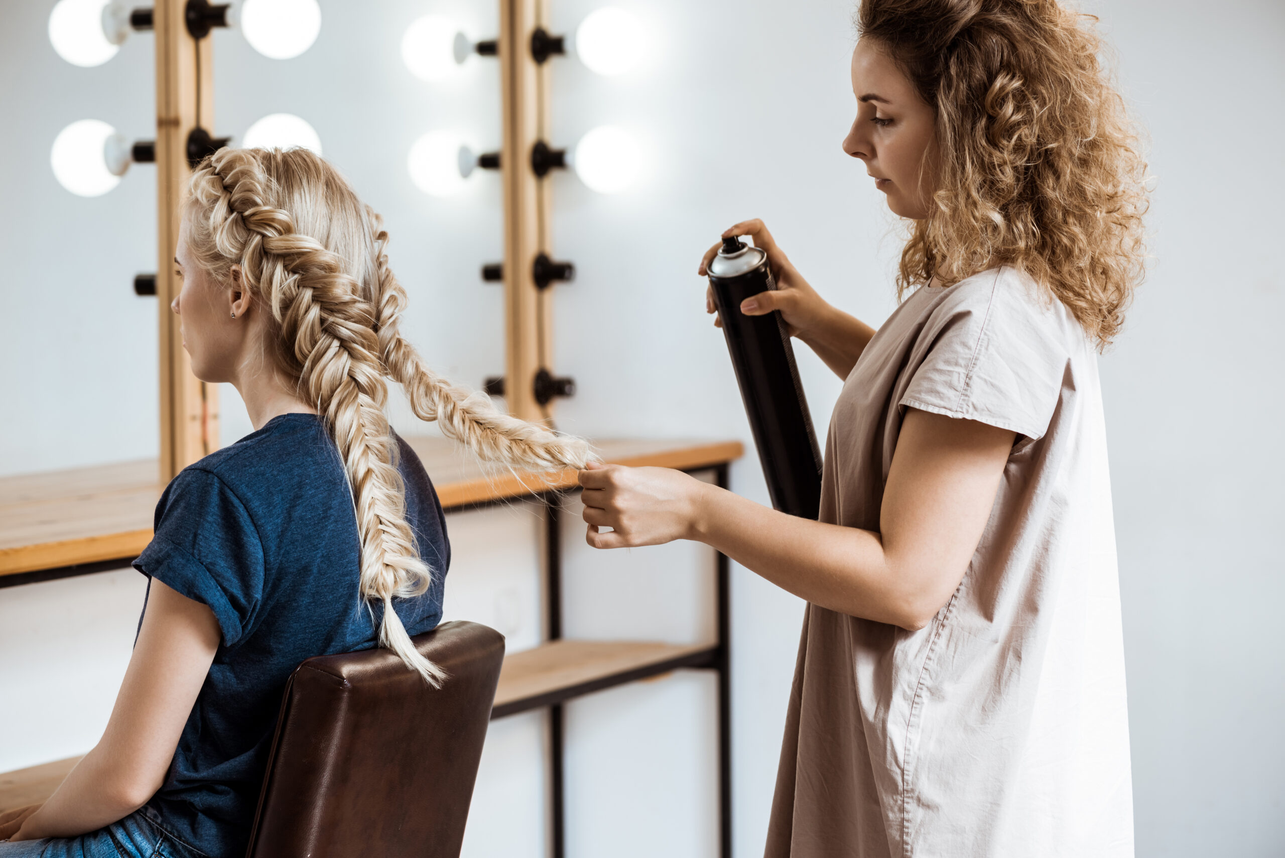 Female hairdresser making hairstyle to blonde girl in beauty salon.